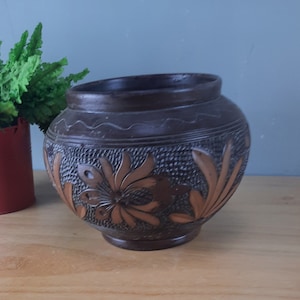 Op de afbeelding: Een donkerbruine keramische plantenpot met een reliëf bloemmotief. Het ontwerp bevat bruine en oranje bloemen en bladeren.