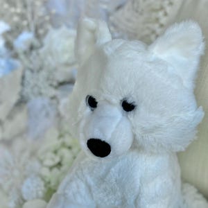 K&ouml;nnte beinhalten: Ein wei&szlig;es Pl&uuml;schtier eines Eisb&auml;ren mit schwarzen Augen und einer schwarzen Nase. Das Stofftier hat eine flauschige Textur und befindet sich vor einem verschwommenen, wei&szlig;en Hintergrund. Die Ohren des B&auml;ren sind aufrecht und sein Fell ist ein helles, sauberes Wei&szlig;.