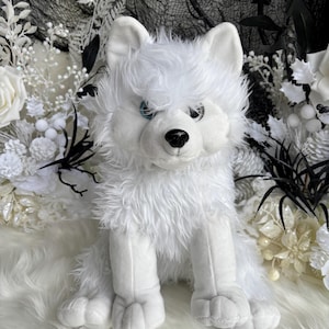 May include: A plush toy of a white wolf with long, shaggy fur, pointed ears, and bright blue eyes. The stuffed animal has a black nose and is depicted in a seated position with its front paws resting forward, showcasing a soft, textured appearance.