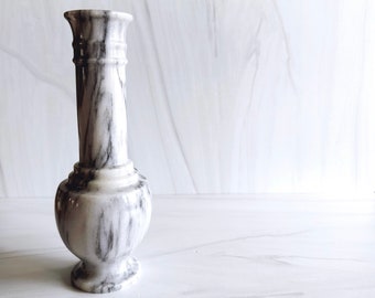 May include: A white marble vase with black veining. The vase has a round body and a narrow neck.