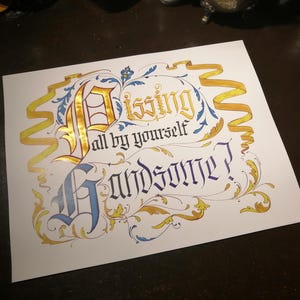 May include: A white card with gold and blue calligraphy that reads "Kissing all by yourself Handsome?" The calligraphy is surrounded by gold and blue floral designs.