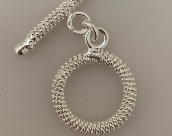 May include: Silver toggle clasp with a textured, round ring and a straight bar. The clasp is designed for jewelry making.