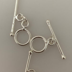 May include: Two silver toggle clasps with round rings. The clasps are made of metal and have a polished finish.