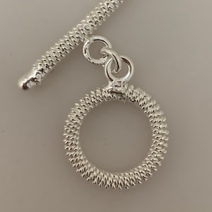May include: Silver toggle clasp with a textured, round ring and a straight bar. The clasp is designed for jewelry making.