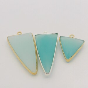 May include: Three triangular pendants in varying sizes. The pendants feature a light blue-green hue and are framed with gold and silver-colored metal. Each pendant has a small loop at the top for attaching to a chain or other jewelry component.