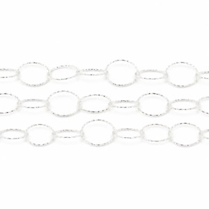 May include: A silver-toned metal chain featuring a repeating pattern of alternating large and small circular links. Each individual link has a textured, shimmering surface that reflects light, creating a consistent metallic appearance throughout.