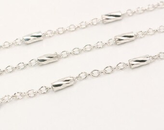 May include: A silver-toned metal chain necklace featuring a series of small, cylindrical beads spaced evenly along the links. The beads have a subtle, twisted, or faceted texture that reflects light, creating a polished and reflective appearance.