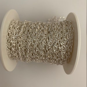 May include: A spool of silver chain, wound tightly around a white cardboard core.