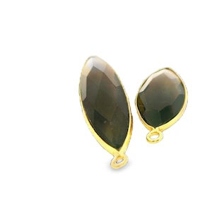 May include: Two gemstone pendants with a gold-colored bezel. One is elongated, the other is a smaller, rounded shape. Both have a dark, faceted interior. The pendants have a small loop for attaching to a chain or other jewelry component.