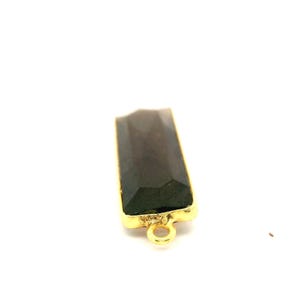 May include: A rectangular, faceted, dark gray gemstone pendant with a gold-colored bezel and a small loop at the bottom. The pendant is set against a white background.
