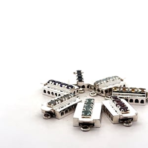 Pode incluir: Um conjunto de seis fechos prateados com pedras preciosas de diferentes cores. Cada fecho tem uma forma retangular com uma fileira de pedras preciosas no centro.