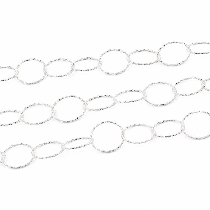 May include: A silver chain necklace featuring a series of interconnected circular links. Each individual link has a textured, shimmering surface that catches the light, creating a continuous, repeating pattern across the length of the jewelry piece.