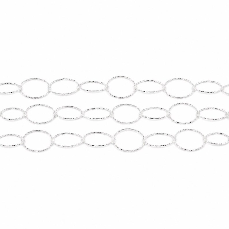 May include: A silver-toned chain featuring three parallel rows of interconnected circular links. Each individual link has a textured, shimmering surface that reflects light, creating a repeating pattern of circles across the entire length of the chain.