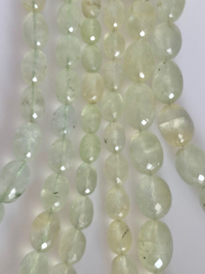 May include: A strand of light green oval-shaped beads. The beads are translucent and have a slightly frosted appearance.