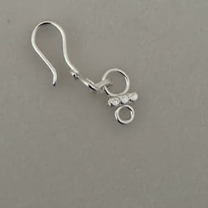 May include: A silver jewellery clasp featuring a hook and a series of small, decorative circles. The clasp is designed for necklaces or bracelets. The hook is curved, and the circles are arranged in a cluster.