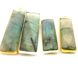 May include: Four rectangular labradorite pendants with gold and silver-colored metal frames. The stones have a mix of blue, green, and gray hues. Each pendant has a small loop at the top for hanging.