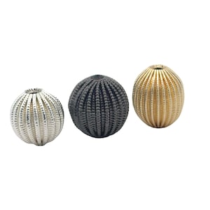 May include: Three round decorative beads with a textured surface. The beads are silver, black, and gold.