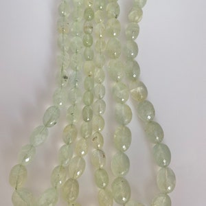 May include: A strand of light green oval-shaped beads. The beads are faceted and have a translucent appearance.