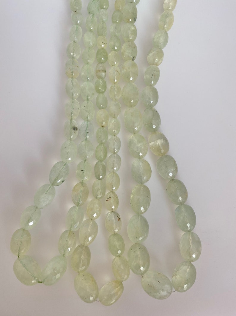 May include: A strand of light green oval-shaped beads. The beads are faceted and have a translucent appearance.