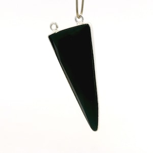 Könnte beinhalten: Ein dreieckiger Anhänger mit einer dunkelgrünen, glänzenden Oberfläche, eingefasst von silberfarbenem Metall. Der Anhänger hängt an einer dünnen, hellfarbigen Kordel, mit einer kleinen Schlaufe oben zur Befestigung.