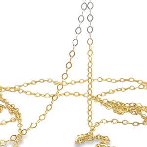 May include: Close-up of delicate gold-colored chain jewelry. The chain is composed of small, interconnected oval links. The chain is displayed against a white background, highlighting its intricate design and metallic sheen. The jewelry appears to be new.