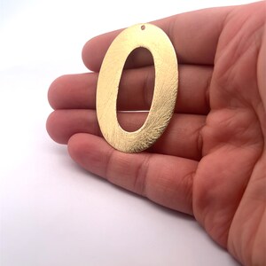 May include: Gold-colored metal number zero charm with a brushed finish and a hole at the top for hanging.