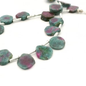 May include: Strands of gemstone beads. Each bead is a flattened, irregular shape, with a teal and magenta color scheme. The beads are strung on a silver-colored wire, creating a necklace or bracelet.