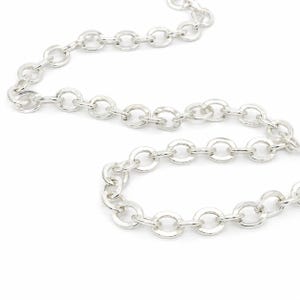 May include: A silver-toned metal chain necklace featuring a series of uniform, circular, interlocking links. The chain is arranged in a curved, flowing pattern, showcasing the reflective, polished surface of each individual round link.