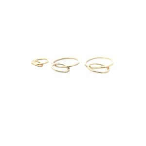 May include: Set of three gold-toned rings with a simple, minimalist design. The rings are interlocking and have a slightly hammered texture.