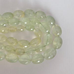 May include: A strand of light green oval-shaped gemstone beads. The beads have a faceted finish and are strung on a clear thread.