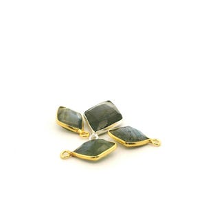 May include: Four gemstone pendants with a diamond shape. The gemstones are a dark gray-green color with a silver and gold setting. The pendants are on a white background.