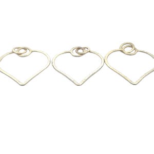 Puede incluir: Tres aros de metal de color dorado en forma de corazón con un círculo más pequeño dentro de cada corazón.