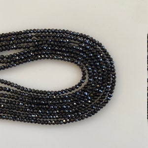 May include: A strand of black faceted beads. The beads are small and round, and they are strung together on a clear thread.