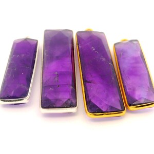 May include: Four rectangular amethyst pendants with faceted surfaces. Two pendants have silver-colored metal frames, and two have gold-colored metal frames. The amethyst stones display varying shades of purple.