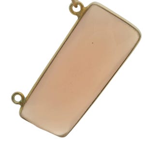 May include: A rectangular pendant necklace with a pale peach-colored stone set in a gold-toned frame. The pendant has a simple, elegant design with a polished finish. The necklace is suspended from a delicate chain.