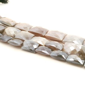 May include: Close-up of three strands of faceted, rectangular beads in shades of grey, beige, and white. The beads have a geometric cut, creating multiple reflective surfaces. The beads are strung together, suggesting jewellery making.