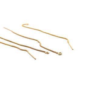 May include: Three gold chain earring extenders. The extenders are made of a delicate box chain and have a small loop at one end and a straight, pointed end at the other.