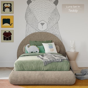 May include: A light green upholstered bed with a curved headboard and a fluffy brown headboard. The bed has a white dinosaur pillow, a green and white striped pillow, and a multi-colored pillow with a geometric pattern. The bed is in a room with a white wall and a drawing of a bear on the wall. The text "Luna Set In Teddy" is written on the wall.