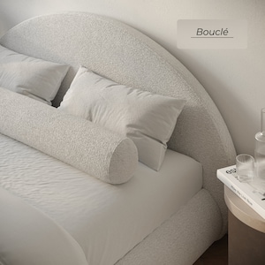 May include: A white bed with a fluffy headboard and a white bolster pillow. The headboard is curved and has a fluffy texture. The bed is made of a soft, white fabric. The text "Bouclé" is written on a white rectangle in the upper right corner of the image.