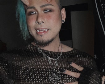 May include: A person with blue hair and devil horns wears a black fishnet sweater with a silver pentagram necklace.