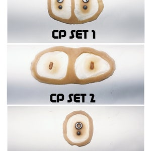 May include: Three close-up images of different sets of prosthetic eyes. The first set has two brown eyes with a silver screw in each. The second set has two brown eyes with a brown dot in each. The third set has one brown eye with a silver screw and a brown dot.