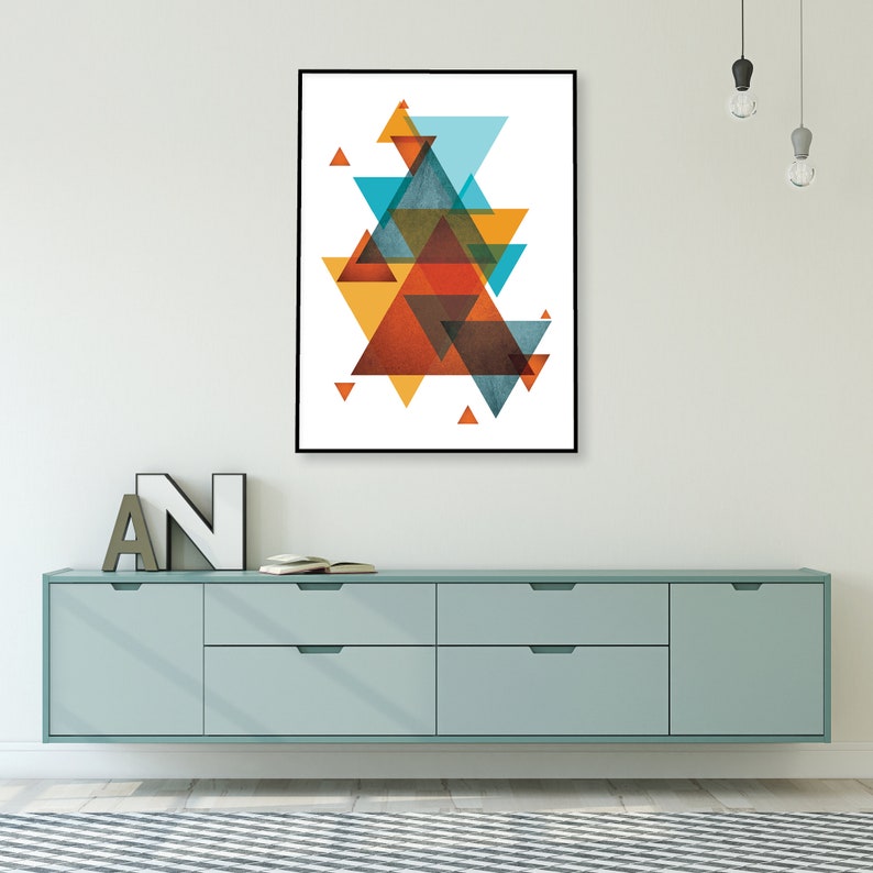 K&ouml;nnte beinhalten: Abstrakter geometrischer Kunstdruck mit einer Komposition aus &uuml;berlappenden Dreiecken in Orange-, Gelb-, Blau- und Braunt&ouml;nen. Der Druck ist in einem schwarzen Rahmen gerahmt und h&auml;ngt an einer wei&szlig;en Wand &uuml;ber einer hellblauen Kommode.
