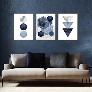 May include: Three abstract geometric prints in shades of blue and gray. The prints are framed and hung on a dark blue wall above a light gray couch.