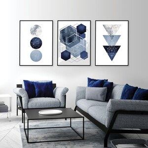 May include: Three abstract geometric wall art prints in a modern style. The prints feature a blue and silver color scheme with geometric shapes and patterns. The prints are framed in black and are hung on a white wall.