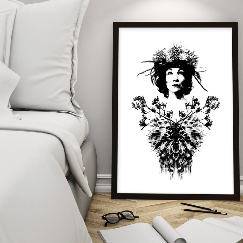 May include: Monochrome art print depicting a woman adorned with a floral headdress and a detailed floral design on the chest. The artwork is framed in a dark brown frame and set against a white backdrop. The print is on a wooden floor.