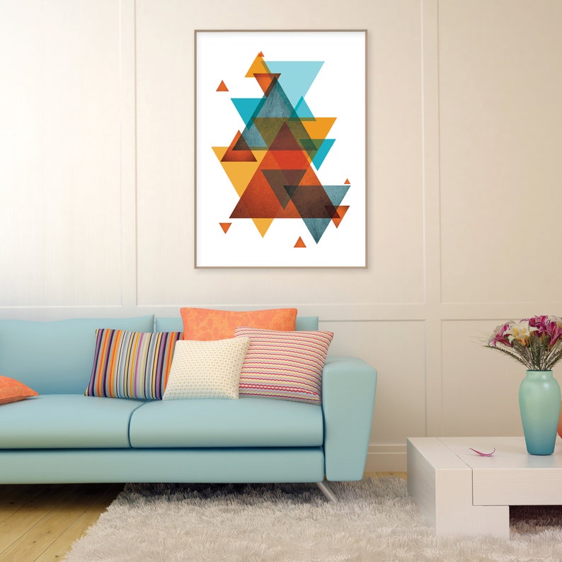 K&ouml;nnte beinhalten: Abstrakter geometrischer Kunstdruck mit einem mehrschichtigen Design aus &uuml;berlappenden Dreiecken in Orange-, Blau- und Braunt&ouml;nen. Der Druck ist gerahmt und an einer wei&szlig;en Wand &uuml;ber einem hellblauen Sofa mit bunten Kissen angebracht.