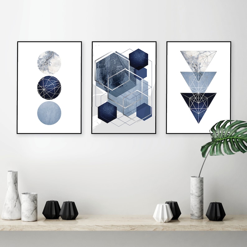 May include: Three framed prints with geometric shapes in shades of blue and silver. The left print features three circles, the middle print features overlapping hexagons, and the right print features three triangles.