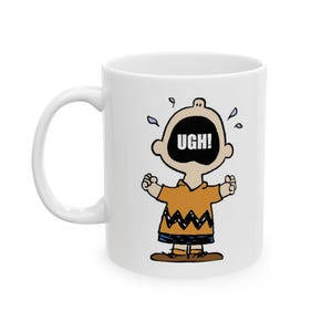 May include: White ceramic coffee mug with a cartoon image of a crying character from the Peanuts comic strip. The character is wearing a yellow shirt with a black zigzag pattern and has the word "UGH!" written across their mouth.