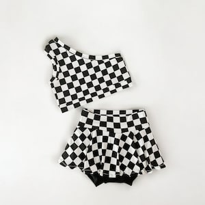 May include: A black and white checkered one-shoulder crop top and matching skirt. The skirt has a ruffled hem.