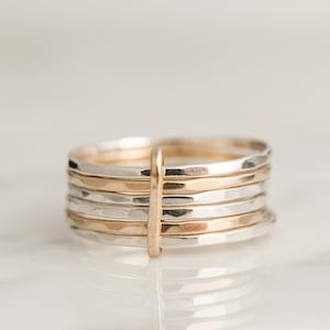 May include: A stack of silver and gold hammered rings. The rings are stacked on top of each other and are all the same width. The rings are a popular style of jewellery.